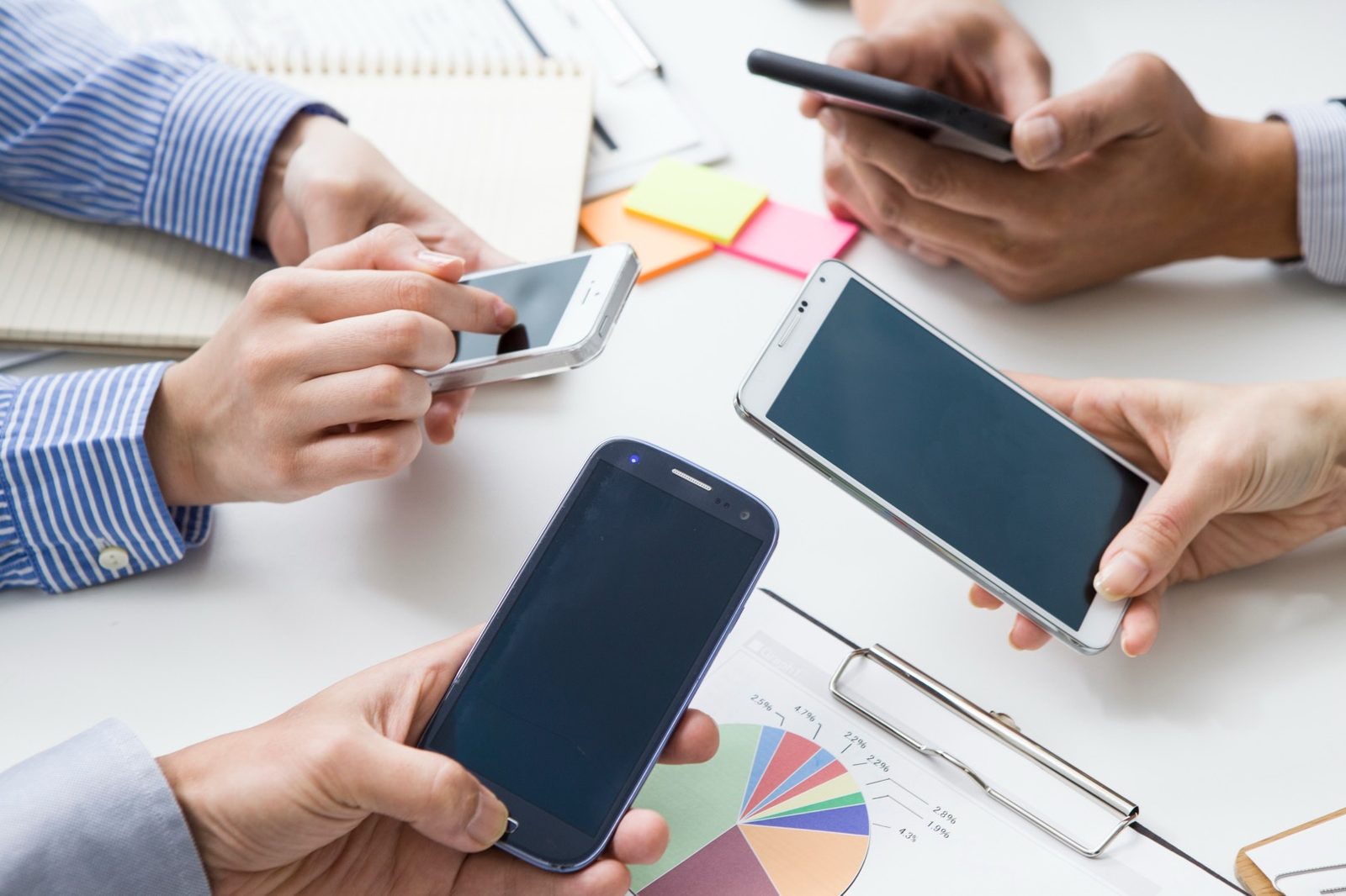 机を囲み、スマートフォンと資料を見ながら打ち合わせる手元